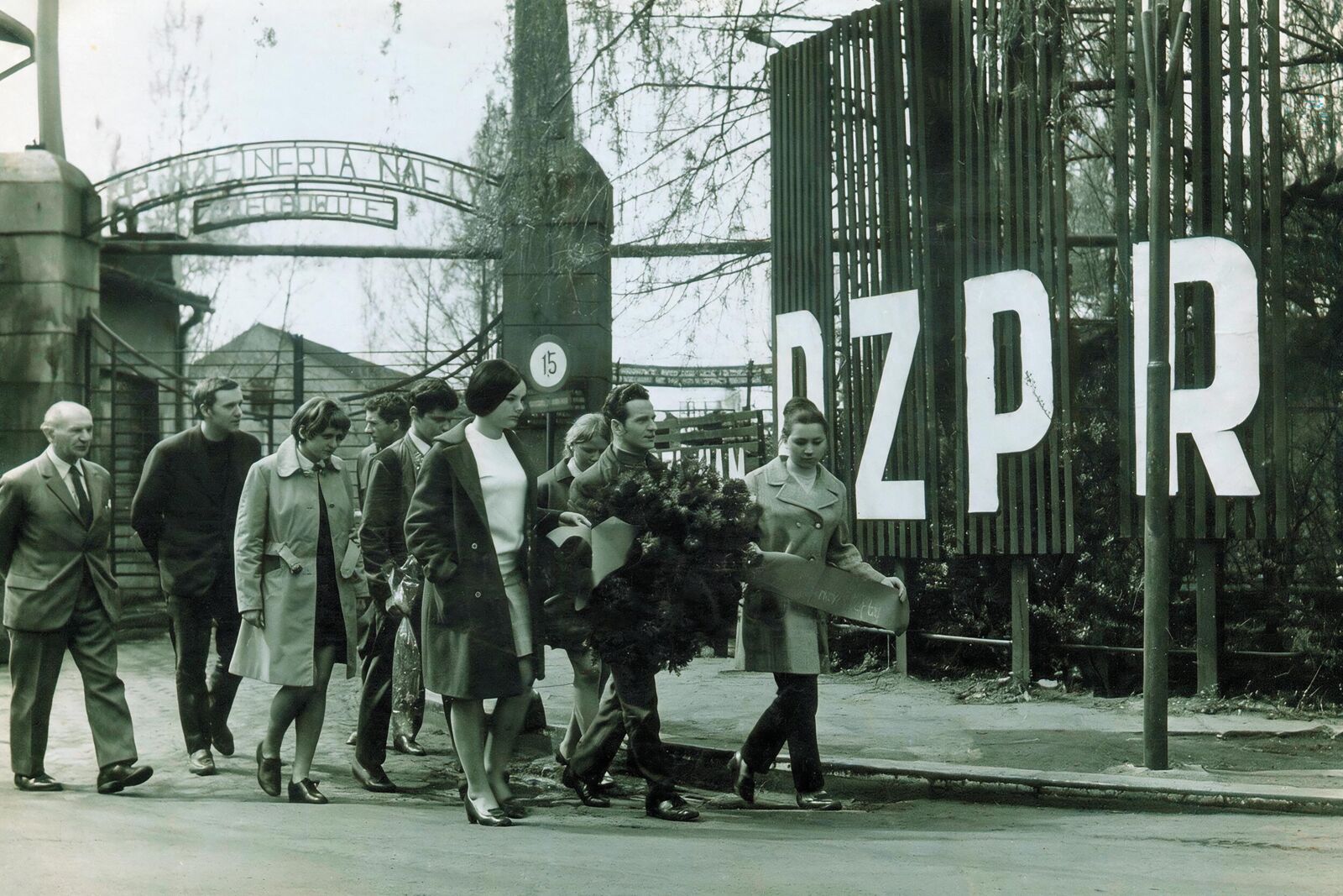 Widok na bramę Śląskich Zakładów Rafineryjnych, delegacja kierownictwa zakładu udaje się z wieńcem pod pomnik zamordowanych więźniów podobozu Tschechowitz I – lata 60. XX wieku