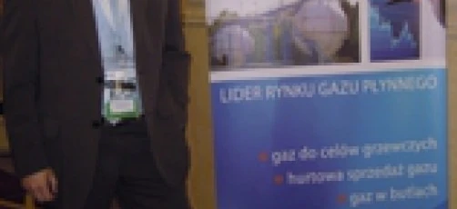 Pracownik biurowy w eleganckim żakiecie i spodniach garniturowych z koszulą i krawatem, reklamujący UNIMOT Gas jako lidera na rynku. Wyraźnie widoczne logo FLF.